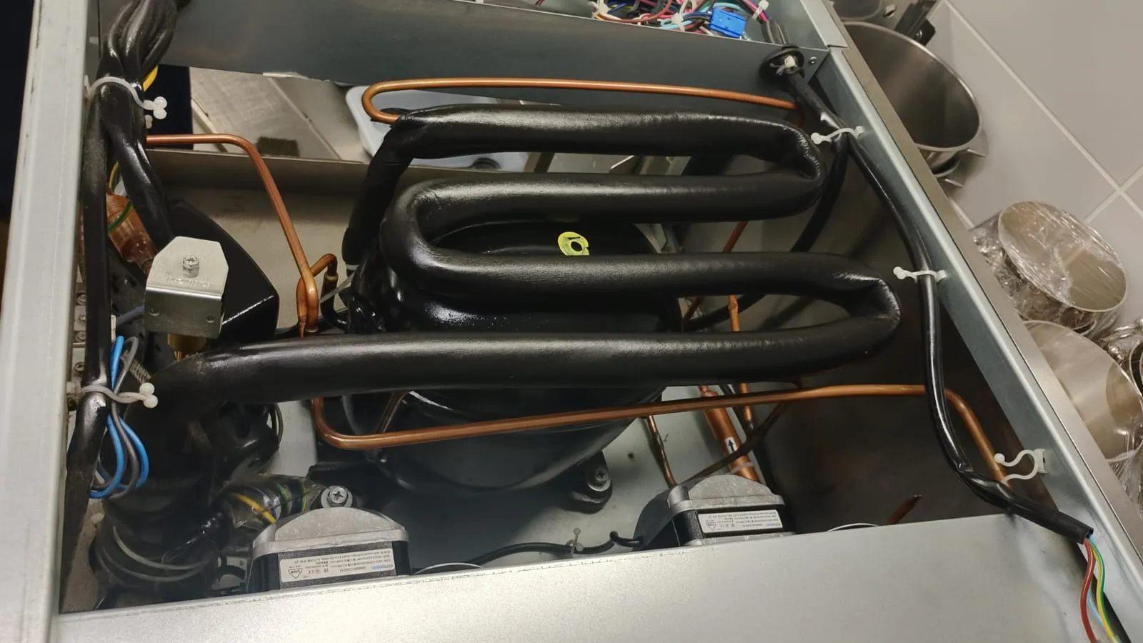 Compressor preto com tubo de sucção coberto por isolamento térmico, tubulação de cobre e dois motores de ventilador
