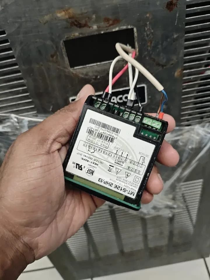 Mão segurando controlador Full Gauge MT-512E com os fios conectados aos bornes
