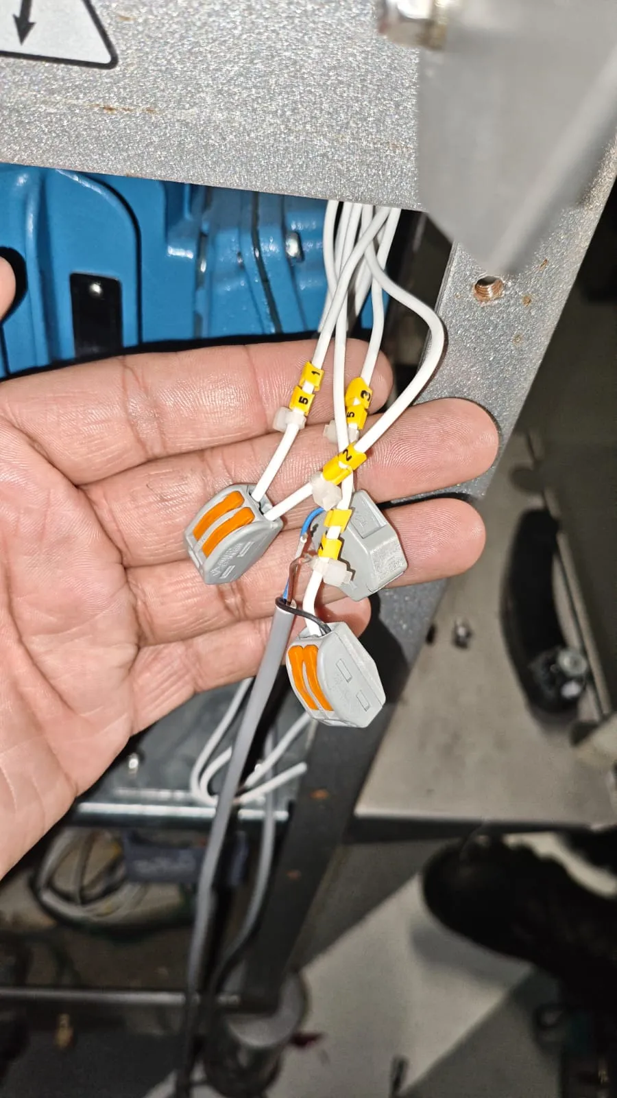 Mão segurando fios brancos com anilhas amarelas numeradas e conectores de alavanca laranja