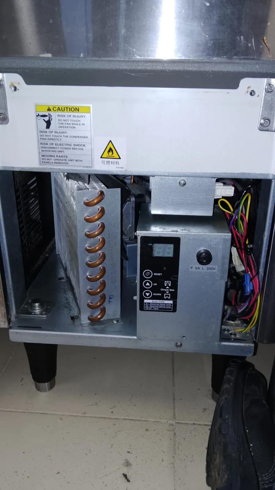 Parte inferior aberta de máquina de gelo, com condensador de cobre e placa de controle com display