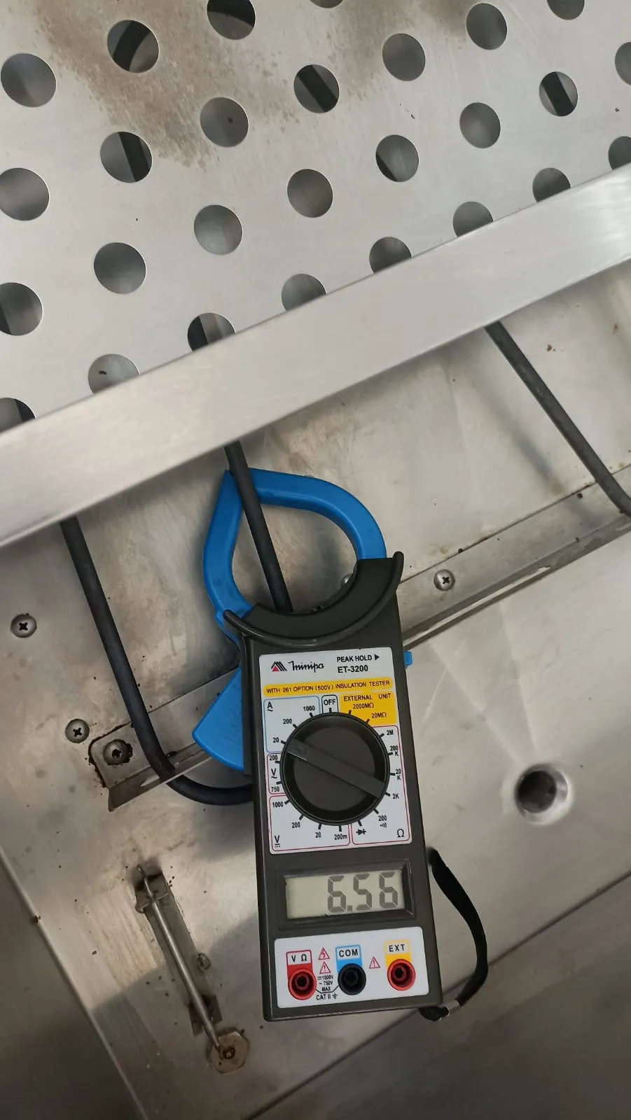 Alicate amperímetro Minipa preso a um cabo dentro de equipamento de inox, com 6,56 no visor