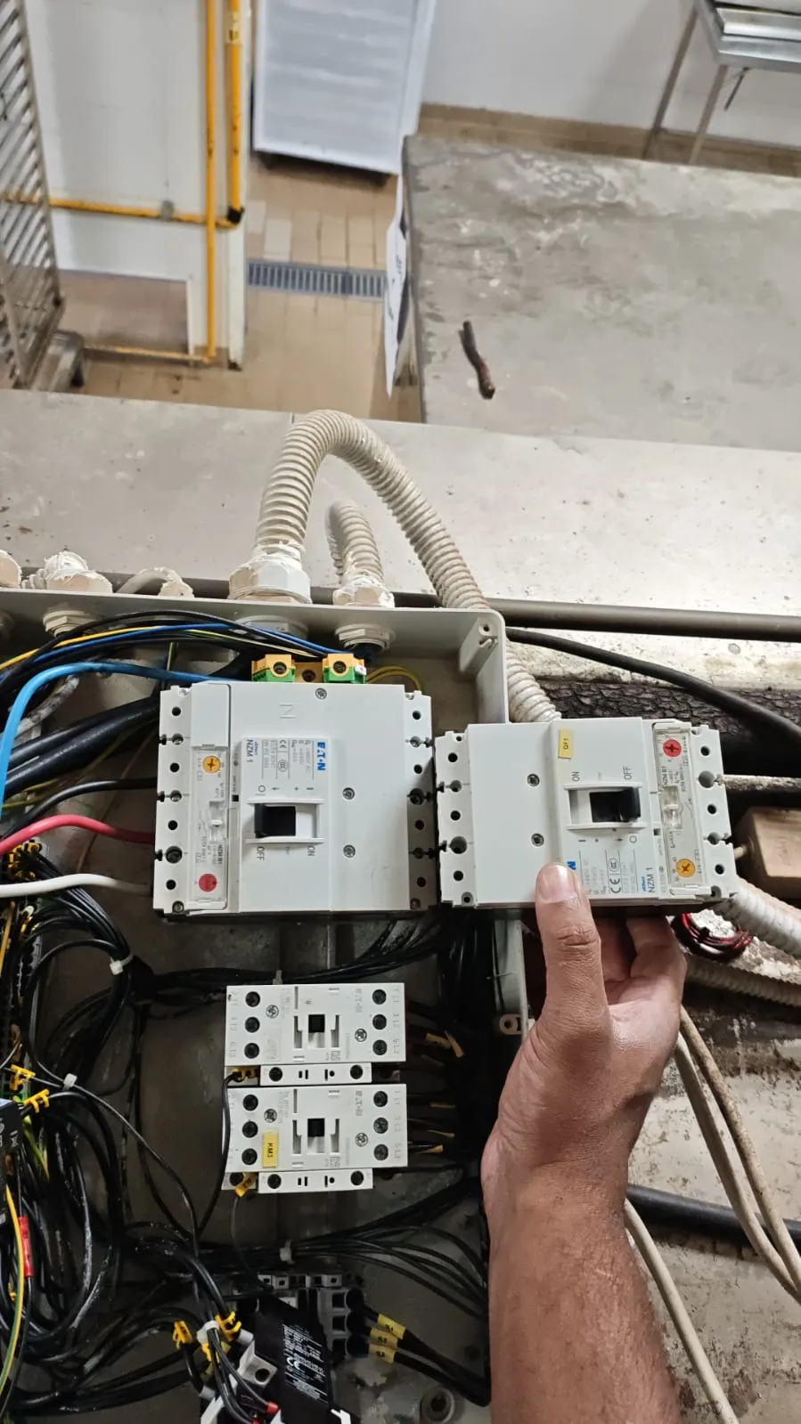 Mão segurando disjuntor Eaton NZM1 ao lado de outro já instalado no quadro de comando