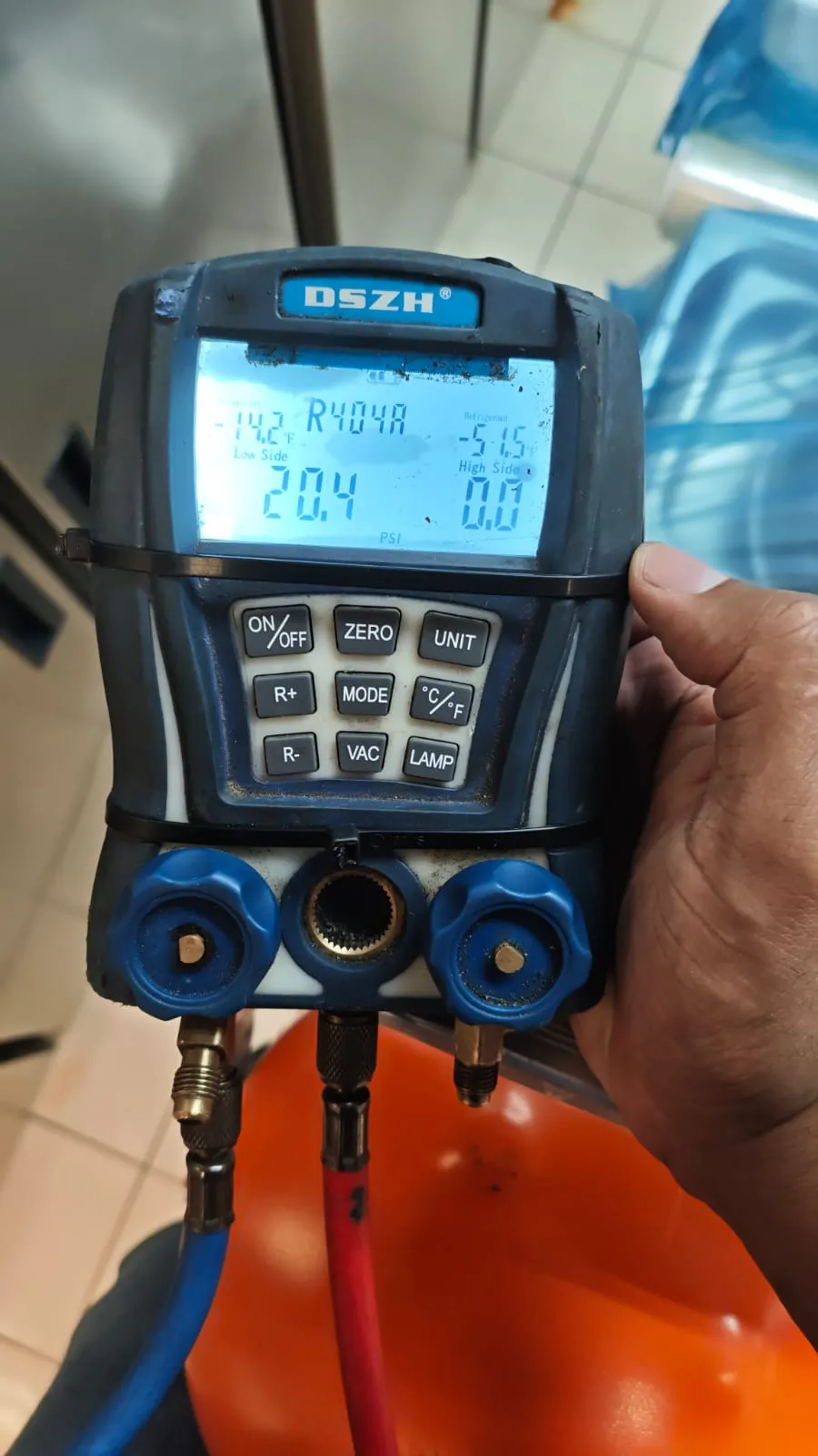 Mão do técnico segurando manifold digital DSZH configurado para R404A, com mangueiras azul e vermelha conectadas